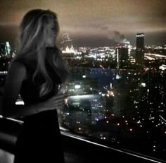 a woman standing in front of a window at night looking out on the city lights