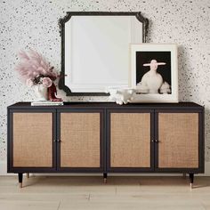 a sideboard with two baskets on it and a mirror above it, in front of a wallpapered background