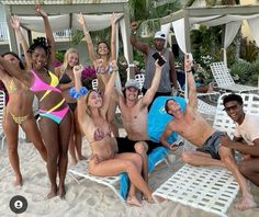 a group of people posing for a photo on the beach with their arms in the air