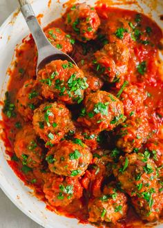 a white bowl filled with meatballs covered in marinara sauce and garnished with parsley