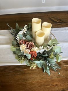 three candles sitting on top of a table with flowers and greenery around the edges