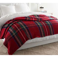 a red and black plaid blanket on top of a white bed with pillows in the background