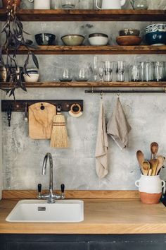 a kitchen sink with wooden shelves above it and dishes on the shelf behind it, along with utensils