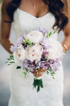 a bride holding a bouquet of white and purple flowers