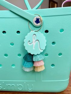 a blue purse with a tassel hanging from it's front loop and a monogrammed letter on the handle