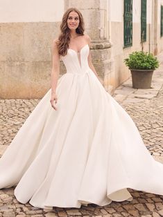 a woman in a white wedding dress standing on a cobblestone street