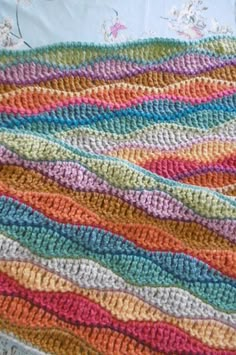 a crocheted blanket with multicolored stripes on it, laying on top of a bed