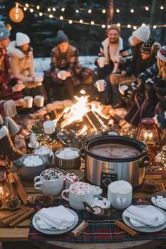 a group of people sitting around a campfire with hot chocolate in front of them