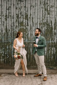 a man and woman standing next to each other in front of a wooden wall with peeling paint