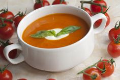 a white bowl filled with tomato soup surrounded by tomatoes