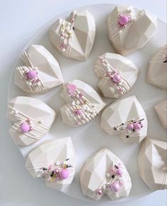 a white plate topped with lots of cakes covered in frosting and pink decorations on top of each other