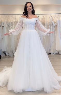 a woman in a white wedding dress standing next to a rack of dresses on display