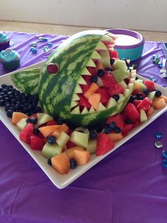 a watermelon cut in half on a plate with grapes, melon and blueberries