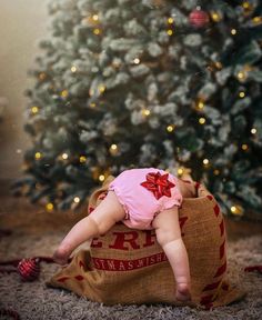 a baby laying on top of a bag in front of a christmas tree