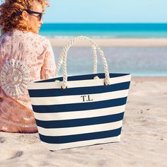 a woman sitting on the beach with a large blue and white striped tote bag