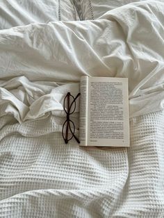 an open book laying on top of a bed with white sheets and pillows next to it