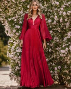 a woman wearing a red dress standing in front of flowers