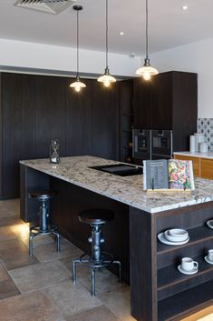 a kitchen with black cabinets and marble counter tops, two bar stools at the island