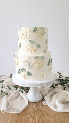 a three tiered cake with white flowers on top and greenery around the edges