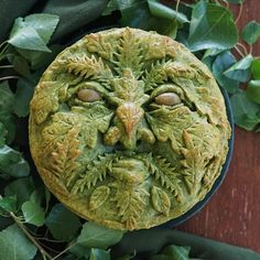 a green face made out of leaves on top of a wooden table next to plants