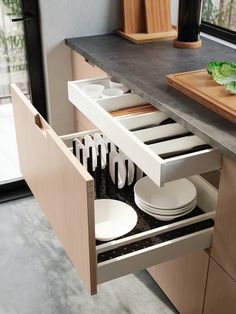 an open drawer in a kitchen with plates and utensils on the counter top