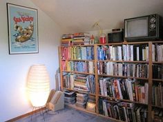 a book shelf filled with lots of books next to a lamp and television on top of it