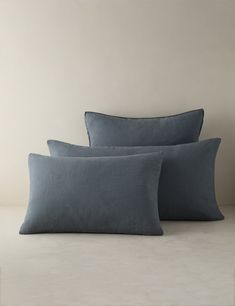 three blue pillows sitting next to each other on a white surface with a beige wall in the background