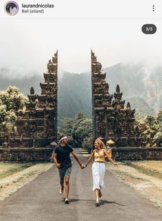 a man and woman walking down a road with an arch in the background holding hands