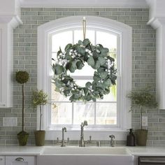 a wreath is hanging on the window sill above a sink in a white kitchen