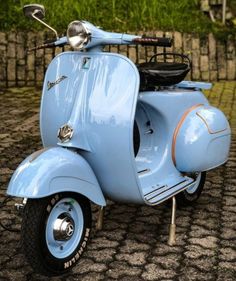 an old blue scooter is parked on the cobblestone pavement in front of a fence