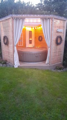 an outdoor jacuzzi in the middle of a yard with curtains on it's sides