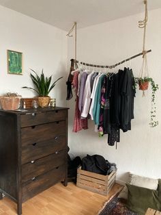 a room with a dresser, clothes rack and potted plant