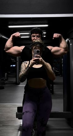 a woman taking a selfie with her cell phone in a gym room while holding a man's arm