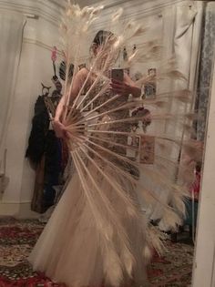 a woman is standing in front of a mirror wearing a dress with feathers on it