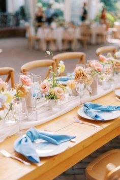 the table is set with plates, napkins and vases filled with colorful flowers