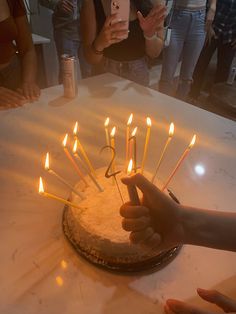 a person holding a phone in front of a cake with lit candles on it and people standing around