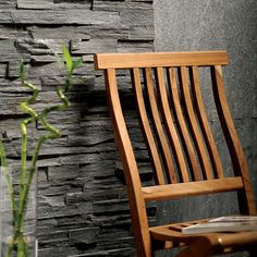 a wooden chair next to a vase with flowers in it and a stone wall behind it