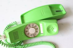 an old style green phone sitting on top of a white table next to a telephone cord