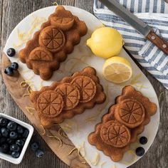 some cookies are on a plate with blueberries and lemons next to the cutting board