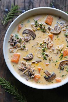 a bowl of soup with mushrooms, carrots and parsley on a wooden table