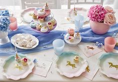 a table topped with plates covered in cupcakes and cake next to vases filled with flowers