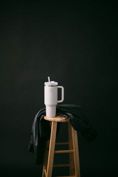 a white coffee cup sitting on top of a wooden stool next to a black blanket