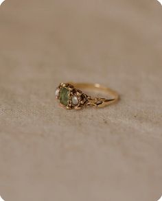 a gold ring with two green stones on the front and side, sitting on a beige surface