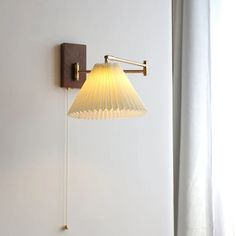 a wall mounted lamp on the side of a white wall next to a window with curtains