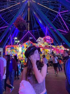 a woman is talking on her cell phone in front of a carnival ride at night