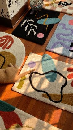 a cat laying on the floor in front of several rugs with different colored designs