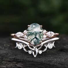 a ring with a green stone surrounded by white diamonds on top of a piece of wood