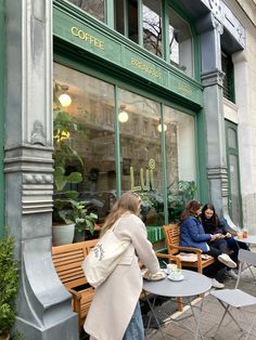 two women sitting at tables in front of a coffee shop with green windows and doors