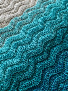 a close up of a knitted blanket on a bed with blue and white colors