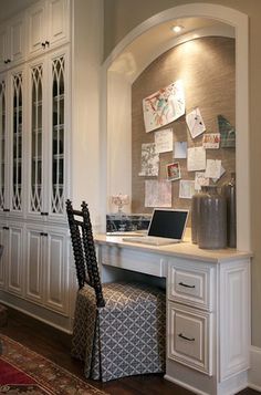 a desk with a laptop on top of it in front of a white cabinet and chair